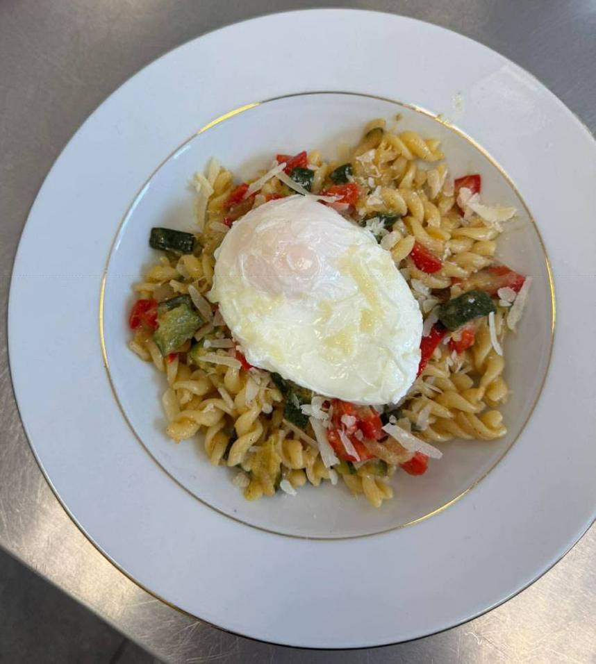 Makaron z duszonymi warzywami i jajkiem poszetowym na talerzu